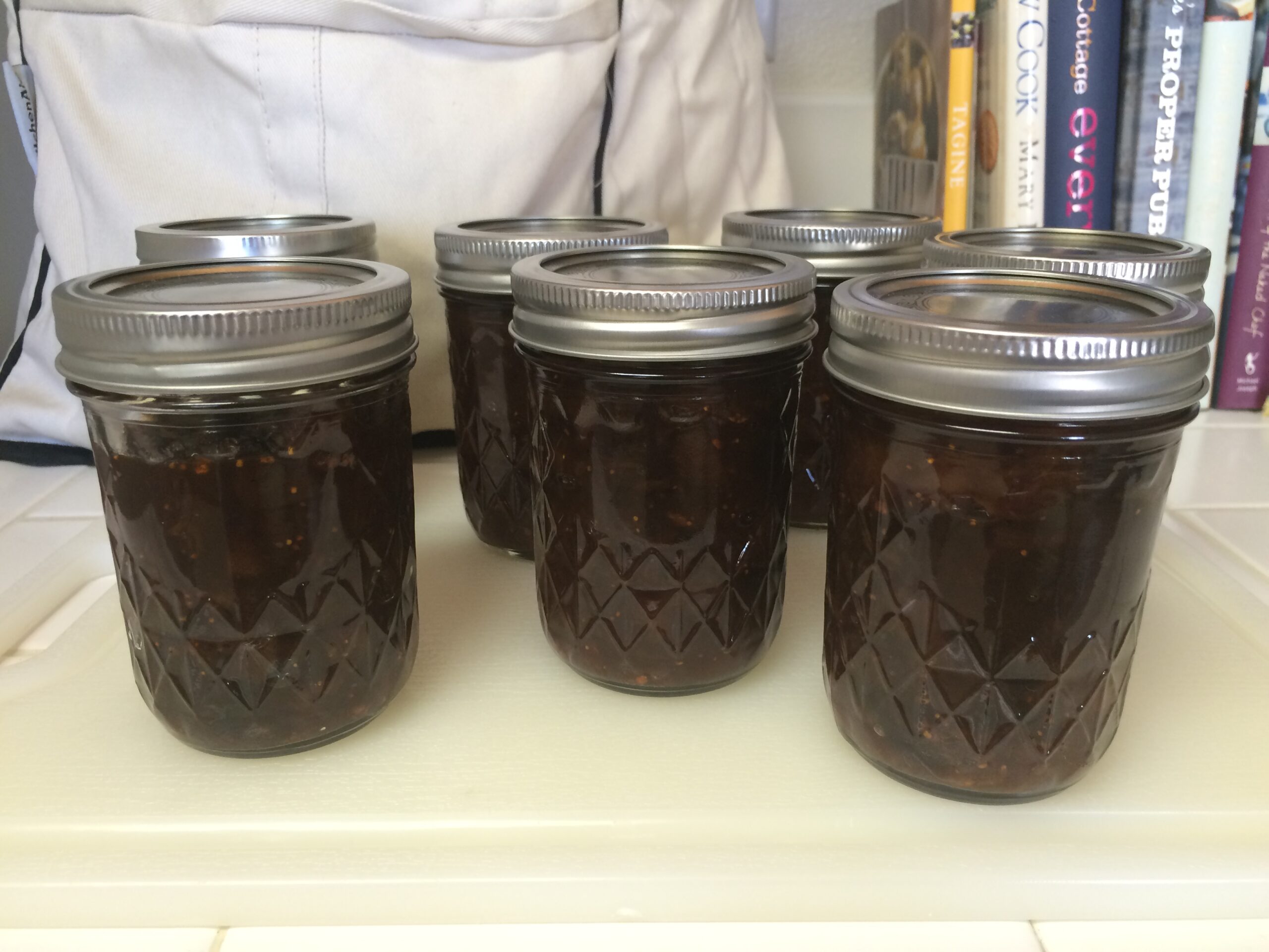 Several jars of homemade apple, pear and fig chutney on a white tiled countertop.